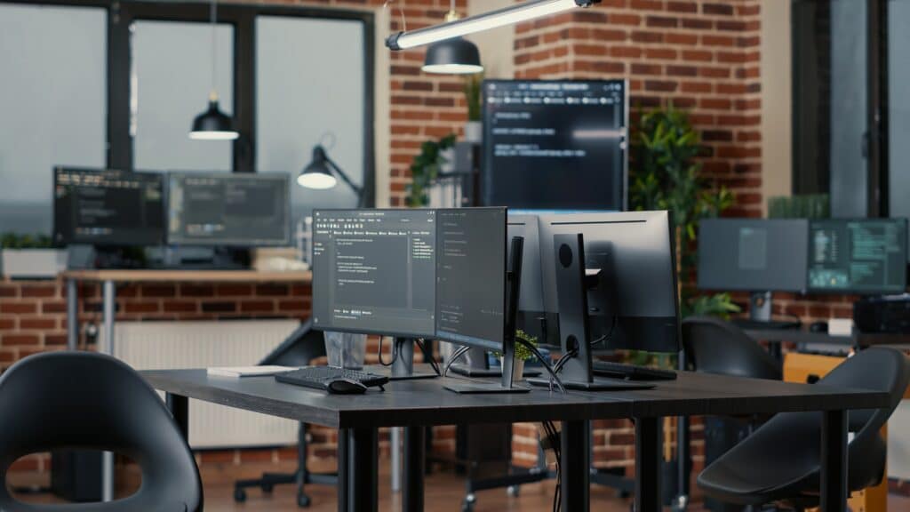 Computer screens running programming code in empty software developing agency office